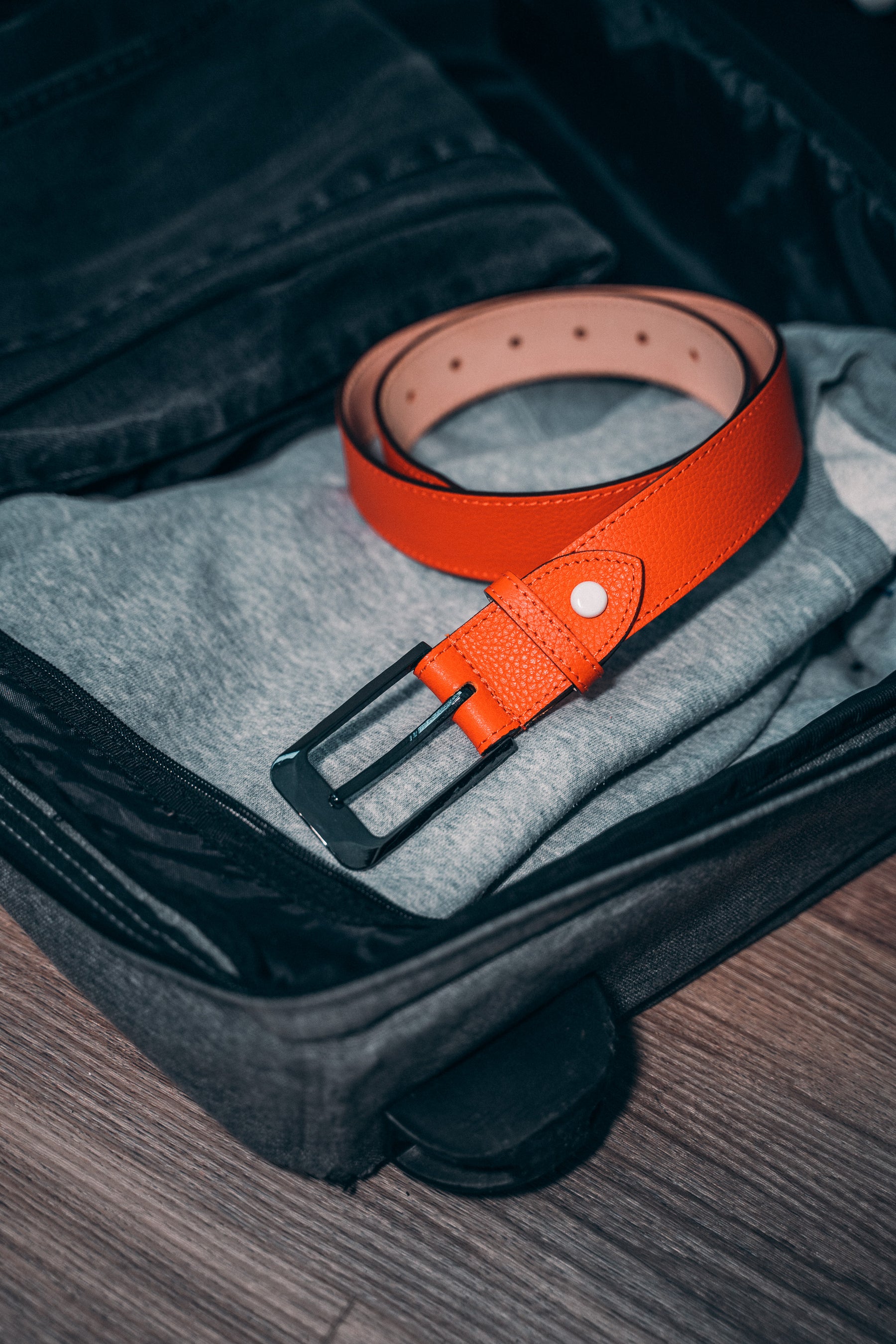 Le modèle MEX en cuir grainé orange est posé élégamment dans une valise prête à partir en voyage avec vous.