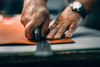 Cette image représente un artisan qui travaille le cuir à l'atelier. Il découpe un cuir lisse pour la ceinture haut de gamme.