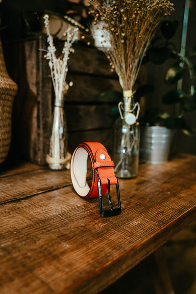 Ceinture artisanale en cuir grainé et en céramique Rozan. Modèle MEX Cuir grainé Orange photo lifestyle disposée sur une table en bois avec des fleurs sèches